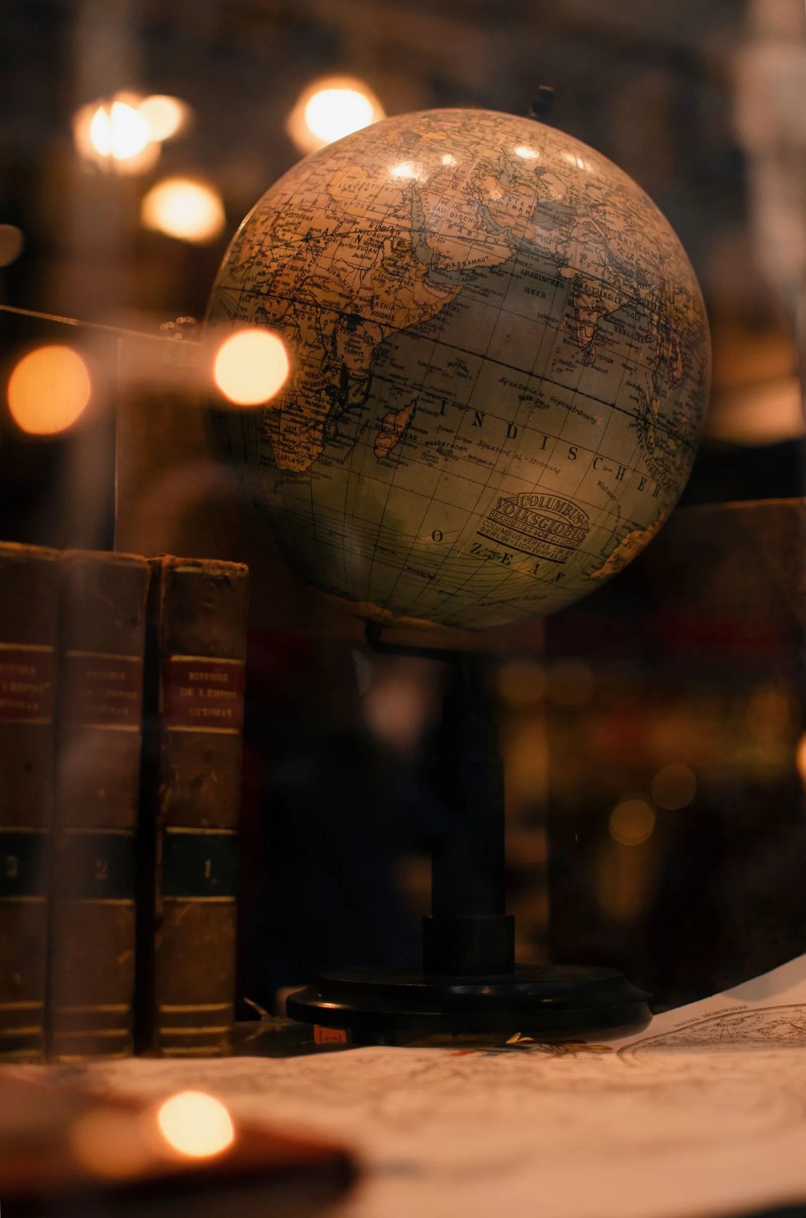 Old leather-bound French books beside a vintage globe under warm library light.
