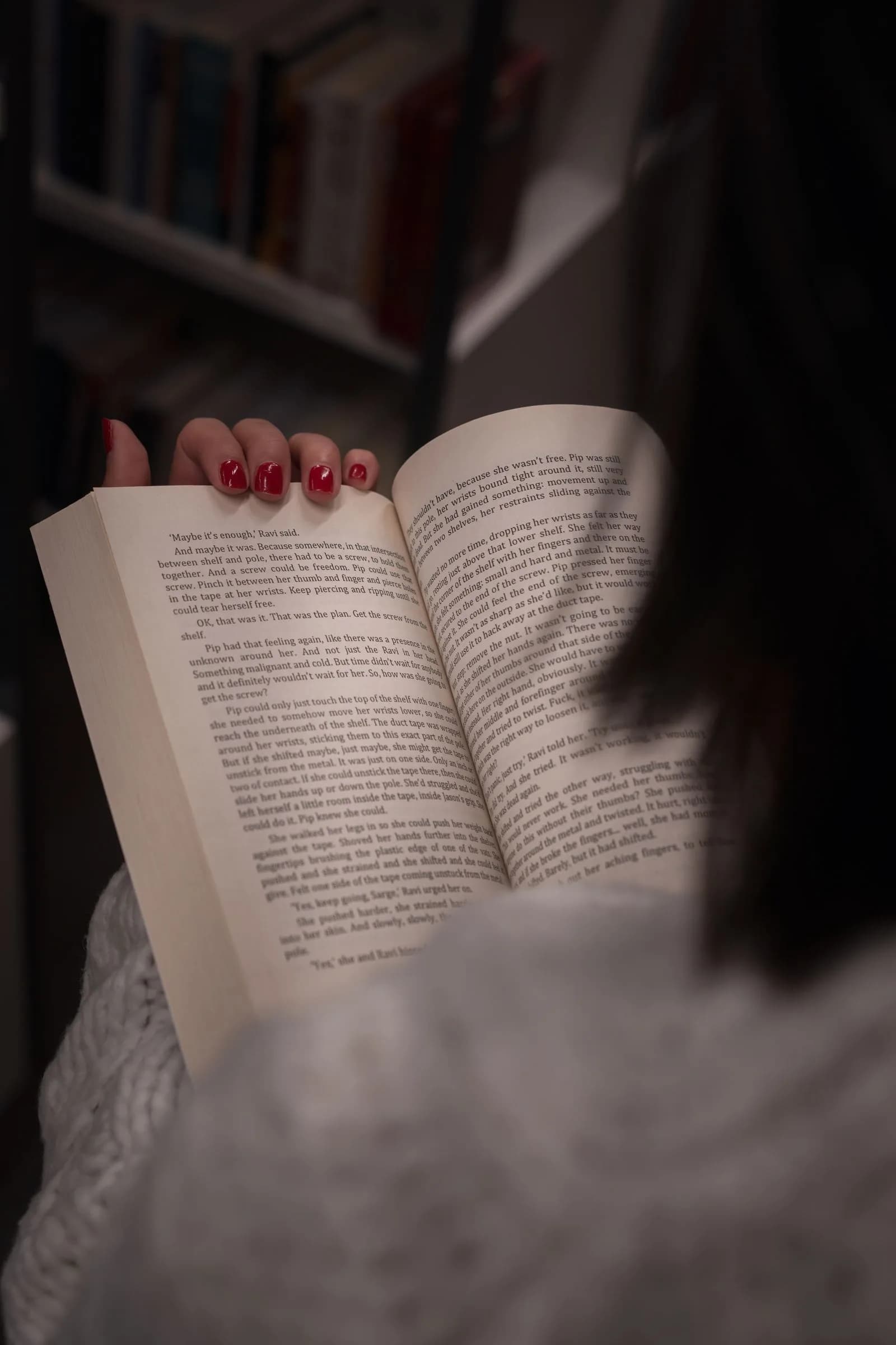 Gros plan sur des mains tenant un livre ouvert dans une bibliothèque tamisée.