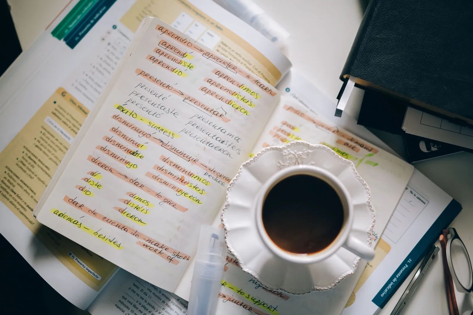 A notebook with hand-annotated Spanish verb conjugations next to a cup of coffee.
