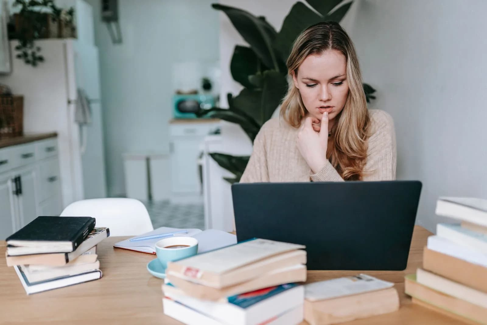 Une personne pensive, entourée de livres, semble bloquée devant son travail de révision.