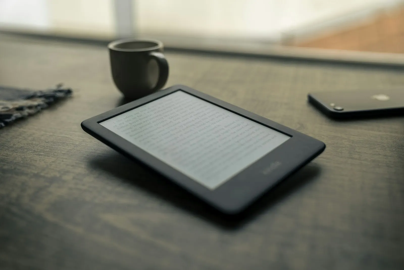 Smartphone resting on a wooden table next to a mug, used for reading and reviewing vocabulary.
