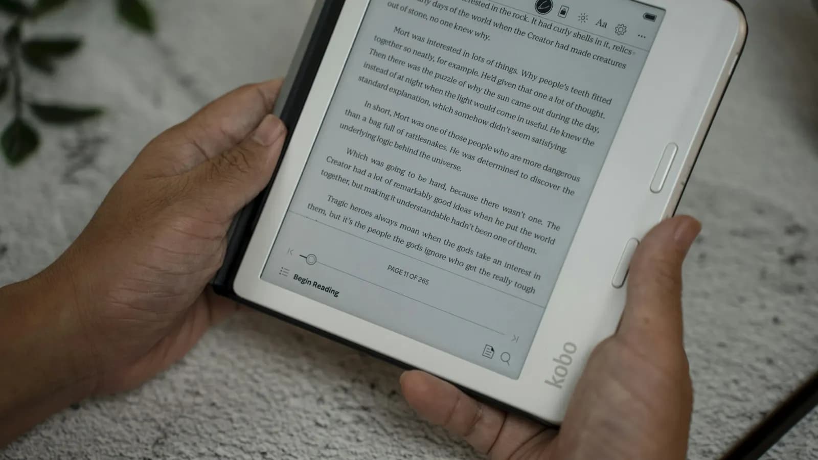 Person holding a digital tablet while reading a book, in bright, natural light.
