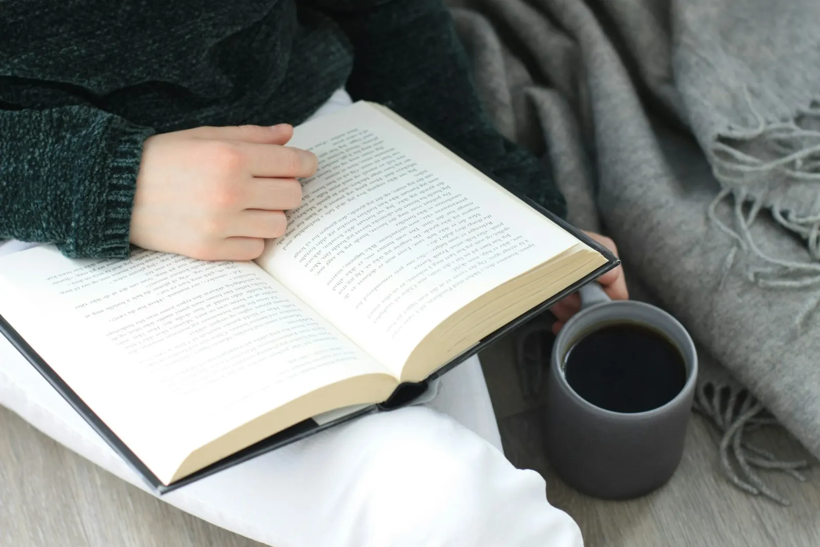 Person sitting with a book and a cup of coffee, reading as part of a daily routine